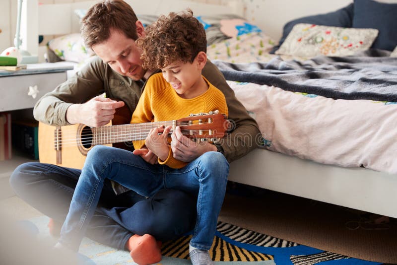 Pai Solteiro Em Casa Com Filho Ensinando-O a Tocar Violão Acústico No Quarto Foto de Stock - Imagem de aprendizagem, casa: 157268350