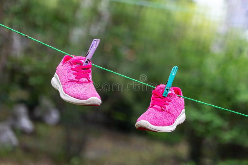 Paia delle scarpe da tennis luminose di forma fisica di sport appese sulla molletta da bucato al cortile dopo la lavanderia all'a fotografie stock libere da diritti Paia delle scarpe da tennis luminose di forma fisica di sport appese sulla molletta da bucato al cortile dopo la lavanderia all'a fotografie stock libere da diritti