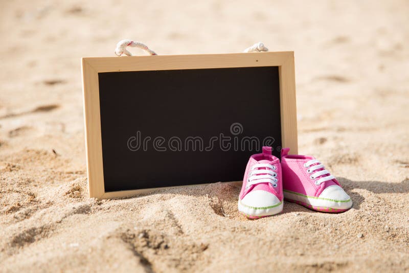 Paia delle scarpe del bambino e di mini bordo di gesso sulla sabbia immagine stock libera da diritti Paia delle scarpe del bambino e di mini bordo di gesso sulla sabbia immagine stock libera da diritti