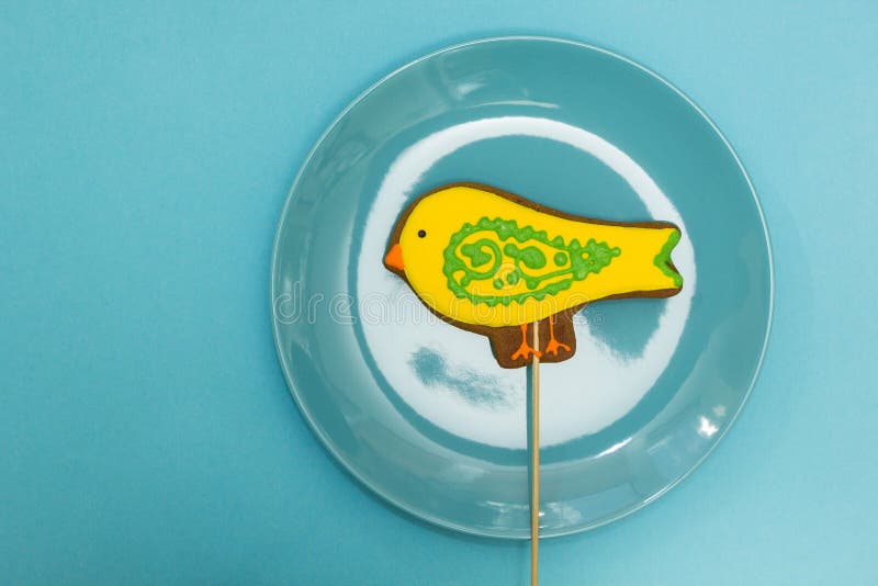Pain d'épice sous forme de “oiseau “jaune dans un plat bleu sur un fond bleu photographie stock libre de droits Pain d'épice sous forme de “oiseau “jaune dans un plat bleu sur un fond bleu photographie stock libre de droits