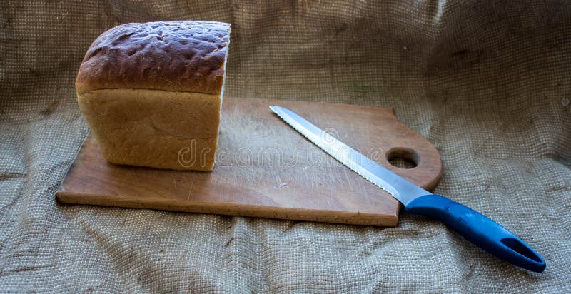 Pain fait maison sur une planche en bois avec un couteau à l'arrière-plan de la toile de jute images stock Pain fait maison sur une planche en bois avec un couteau à l'arrière-plan de la toile de jute images stock