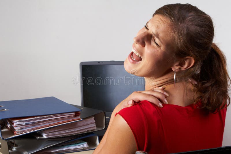 Young woman sitting at her laptop with a lot of work in front of her. She has a pain in her neck / back. Young woman sitting at her laptop with a lot of work in front of her. She has a pain in her neck / back.