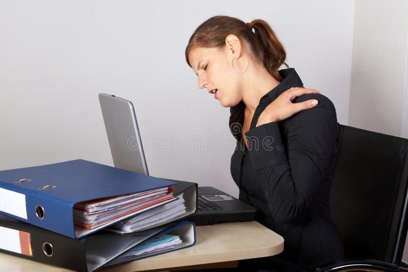 Young woman sitting at her laptop with a lot of work in front of her. She has a pain in her neck / back. Young woman sitting at her laptop with a lot of work in front of her. She has a pain in her neck / back.