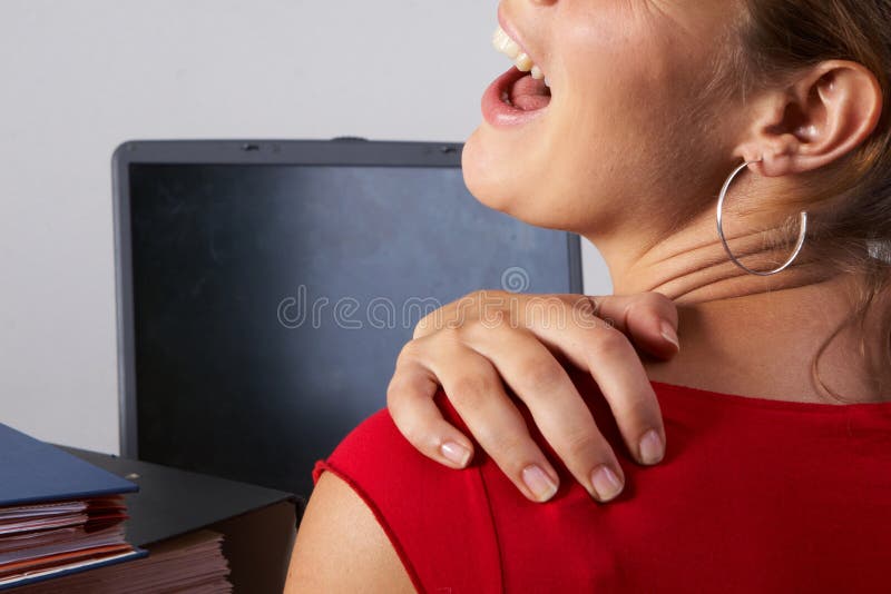 Young woman sitting at her laptop with a lot of work in front of her. She has a pain in her neck / back. Young woman sitting at her laptop with a lot of work in front of her. She has a pain in her neck / back.