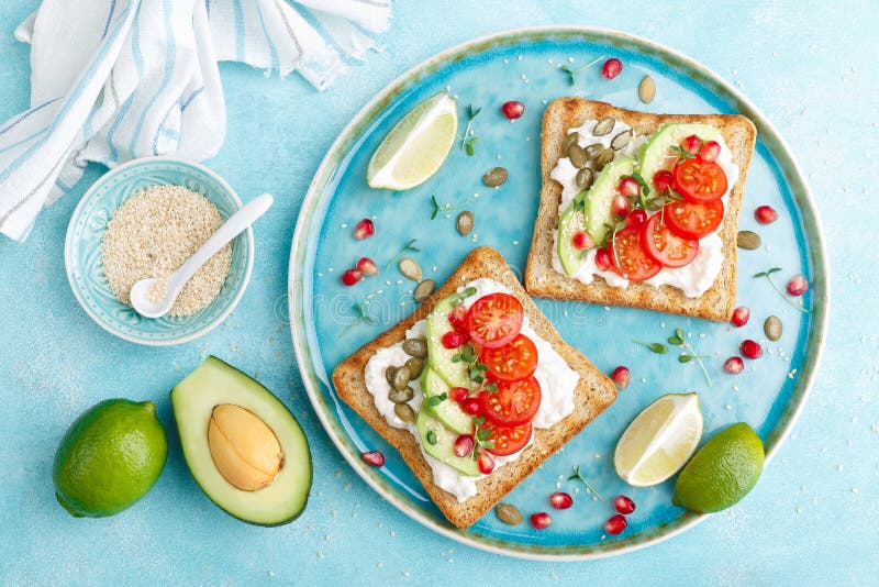 Toasts with feta cheese, tomatoes, avocado, pomegranate, pumpkin seeds and flaxseed sprouts. Diet breakfast. Delicious and healthy food. Flat lay. Top view. Toasts with feta cheese, tomatoes, avocado, pomegranate, pumpkin seeds and flaxseed sprouts. Diet breakfast. Delicious and healthy food. Flat lay. Top view