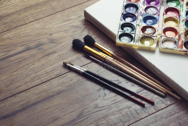 Paint Brushes In Blank Canvas On Wooden Background