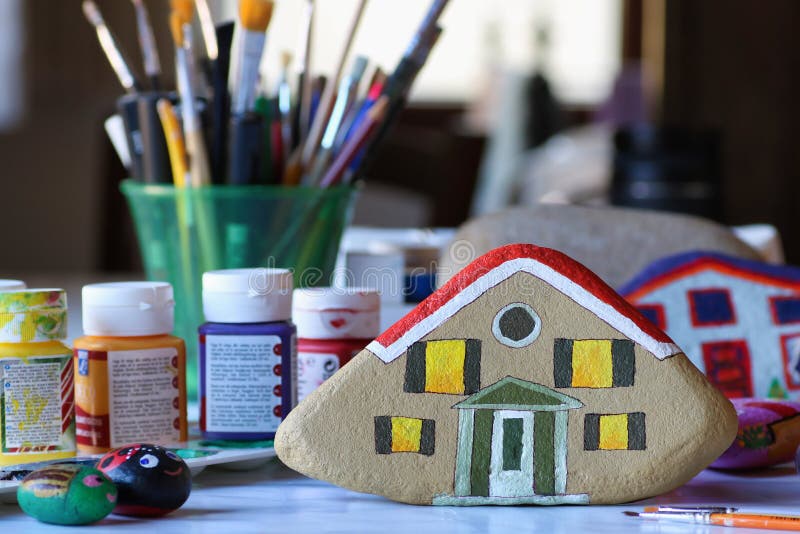 Painted stone in the shape of home, brushes and acrylic colors royalty free stock image