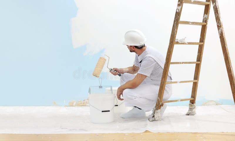 Painter man at work takes the color with paint roller from the bucket and look the wall, copy space template royalty free stock photo