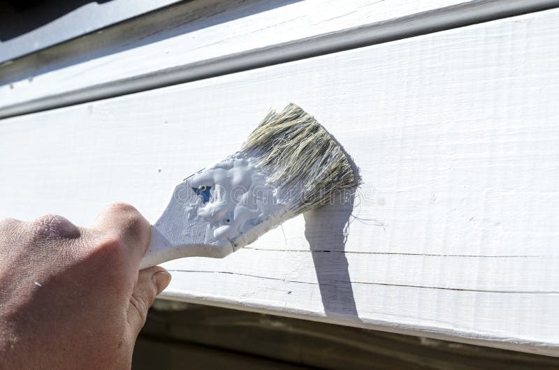 Painter paints a piece of wooden wall with a small brush and white paint, the Builder stock image Painter paints a piece of wooden wall with a small brush and white paint, the Builder stock image