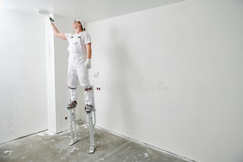 Painter worker on stilts with roller painting ceiling into white