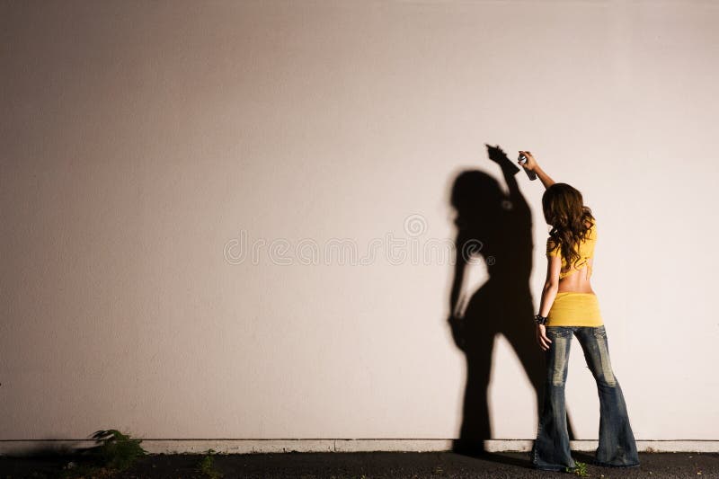 Una giovane donna che dipinge graffiti su un muro con disco illuminazione drammatica.