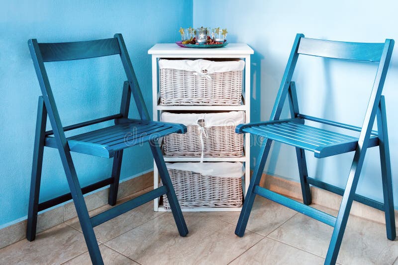 Pair of blue wooden chairs and small white commode near the wall.