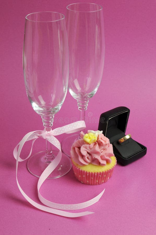 Pair of champagne flute glasses with pink cupcake and wedding ring