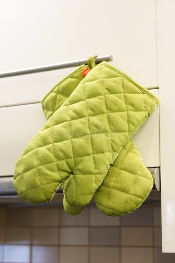 Pair of Green Kitchen Gloves Hanging on a Cupboard Handle. Editorial