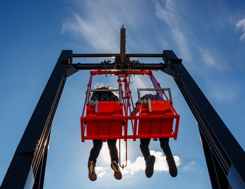 Pair having fun in swing on a high building against blue sky