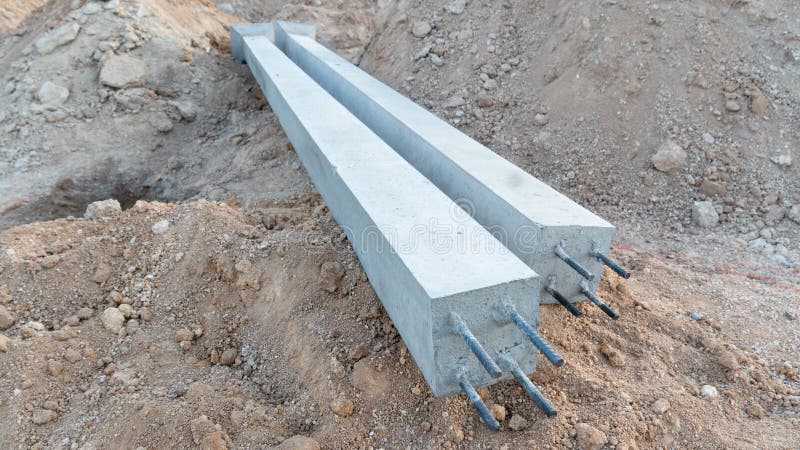 Pair of long square precast concrete pillars resting horizontally on a mound of excavated earth at a construction site. Pillars have exposed steel rebar ends at the front. Load structural stock images, royalty-free photos and pictures