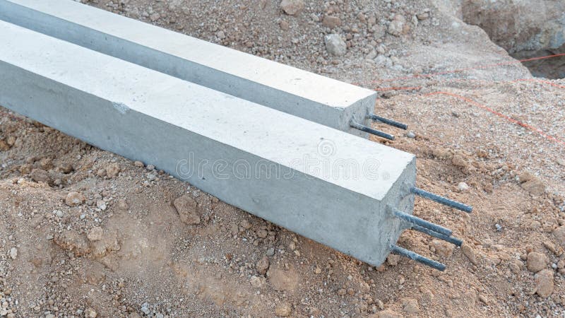 Pair of long square precast concrete pillars resting horizontally on a mound of excavated earth at a construction site. Pillars have exposed steel rebar ends at the front. Load structural stock images, royalty-free photos and pictures