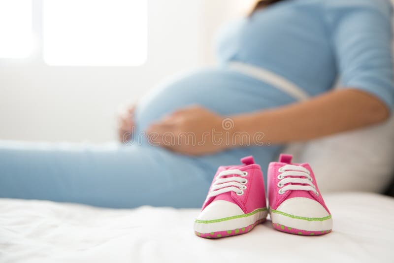 A pair of pink toddler sneakers beside a pregnant woman, focus o