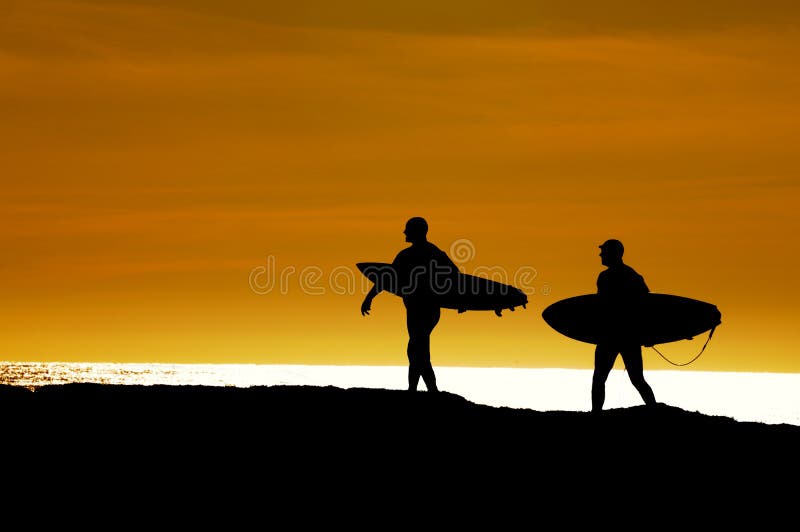 Pair of surfers heading out in the sunset