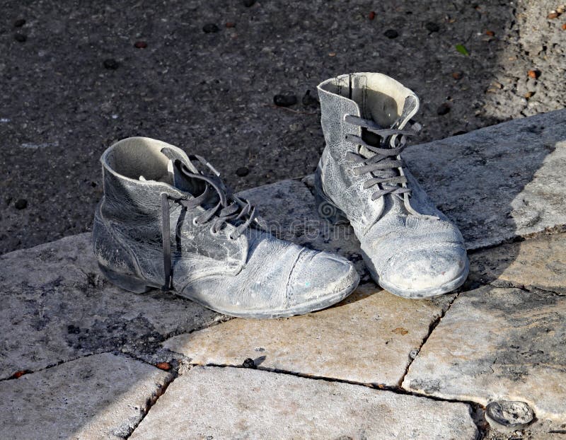 A pair of very old and worn out black boots on the pavement.