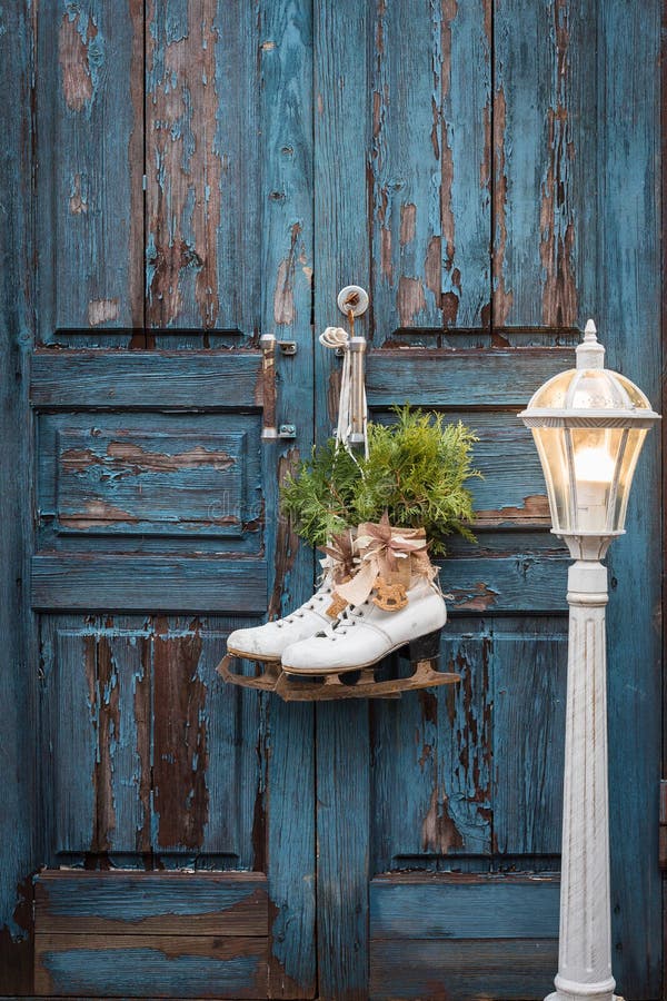 Pair of vintage white Ice Skates with Christmas decoration hanging on the blue rustic door and a big lantern