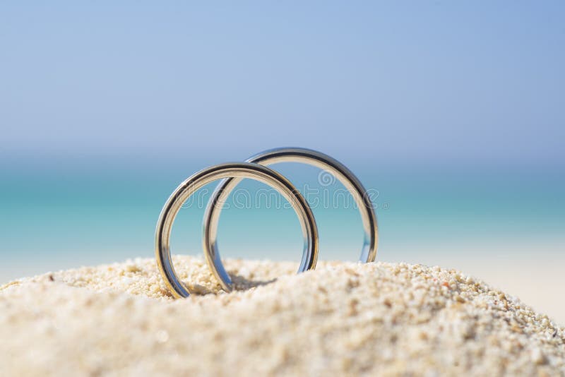 Pair wedding rings in sand on tropical beach