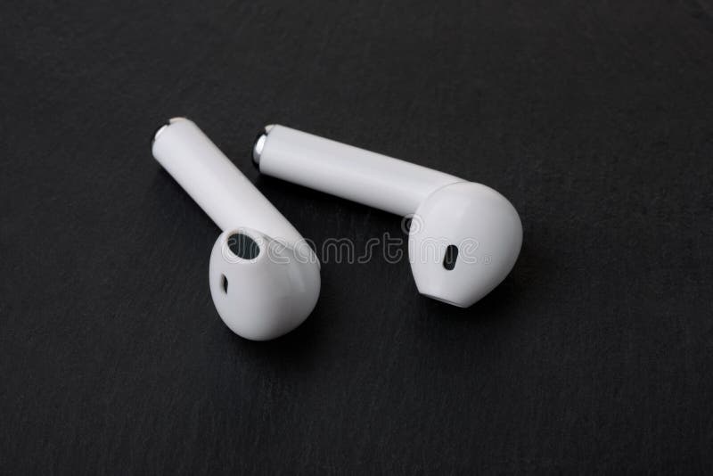 Pair of white true wireless earbuds on black stone background. Pair of white true wireless earbuds on black stone background