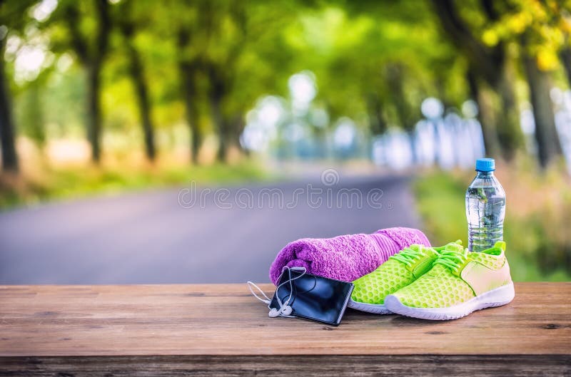 Pair of yellow green sport shoes towel water smart pone and headphones on wooden board. In the background forest or park trail. royalty free stock images Pair of yellow green sport shoes towel water smart pone and headphones on wooden board. In the background forest or park trail. royalty free stock images