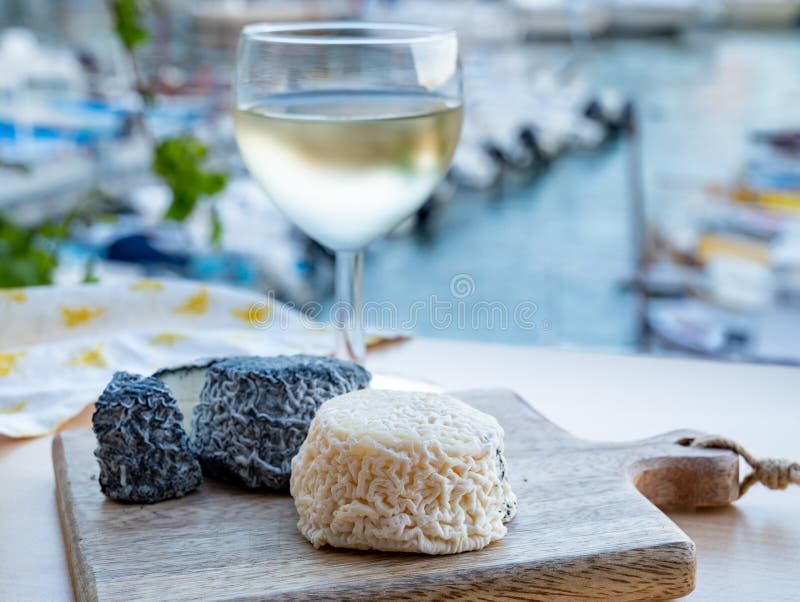 Pairing of French goat cheese crottin and glass of white French wine served with view on boats in harbor of Cassis, Provence