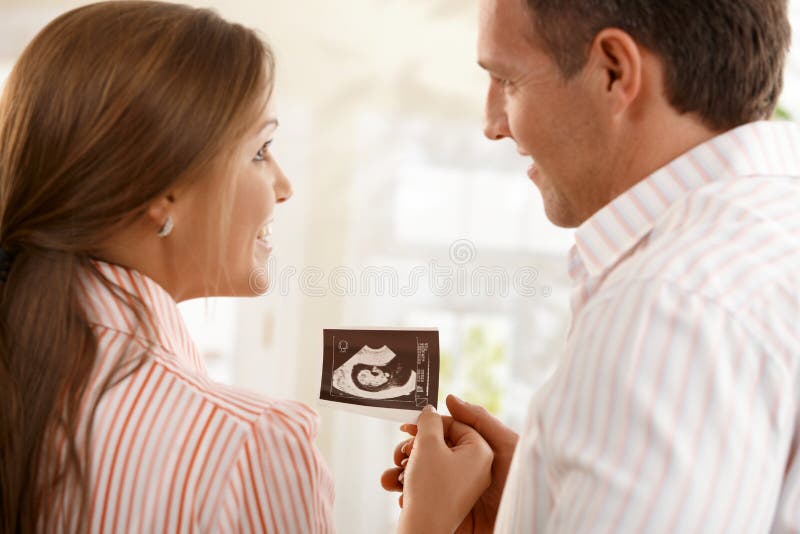 Pais felizes com a foto do bebê do ultra-som fotografia de stock Pais felizes com a foto do bebê do ultra-som fotografia de stock