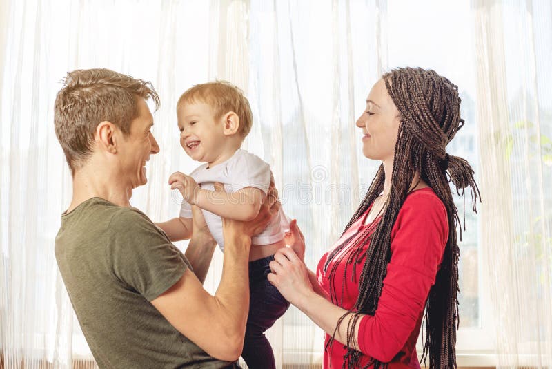 Pais felizes pai e mãe que jogam com o filho do bebê no na manhã no fundo da janela Fam imagens de stock royalty free Pais felizes pai e mãe que jogam com o filho do bebê no na manhã no fundo da janela Fam imagens de stock royalty free