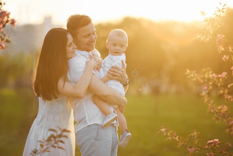 Pais novos bonitos e seu filho pequeno bonito que abraçam e que sorriem no por do sol fotografia de stock royalty free Pais novos bonitos e seu filho pequeno bonito que abraçam e que sorriem no por do sol fotografia de stock royalty free