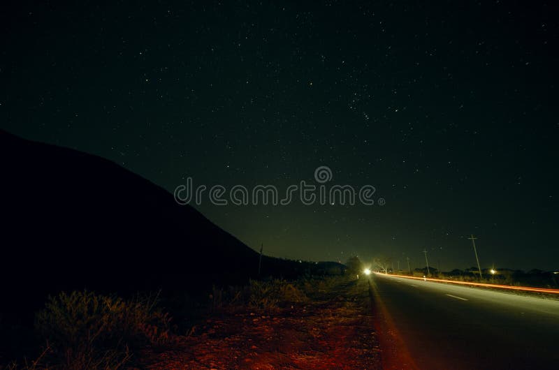 A paisagem bonita da noite das estrelas na silhueta do céu e da montanha perto da estrada com carro arrasta Estrada nas montanhas foto de stock royalty free A paisagem bonita da noite das estrelas na silhueta do céu e da montanha perto da estrada com carro arrasta Estrada nas montanhas foto de stock royalty free