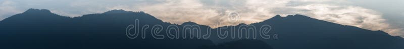 Paisagem da montanha do panorama na silhueta com o céu nebuloso wispy na hora azul fotografia de stock Paisagem da montanha do panorama na silhueta com o céu nebuloso wispy na hora azul fotografia de stock
