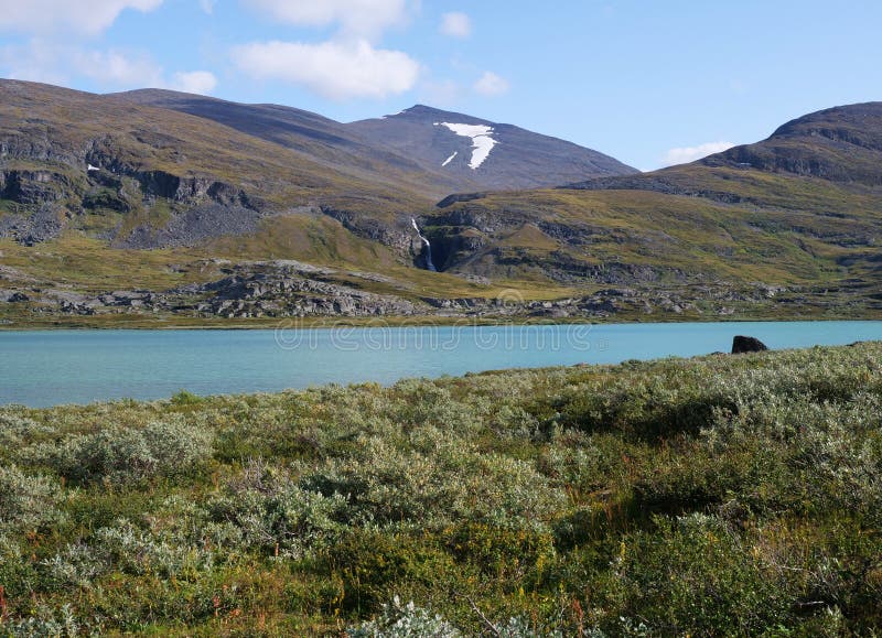 Paisagem natural da Lapónia com o lago glacial azul Allesjok próximo de Alesjaure, floresta de árvores de pássaros, montanhas com imagem de stock Paisagem natural da Lapónia com o lago glacial azul Allesjok próximo de Alesjaure, floresta de árvores de pássaros, montanhas com imagem de stock