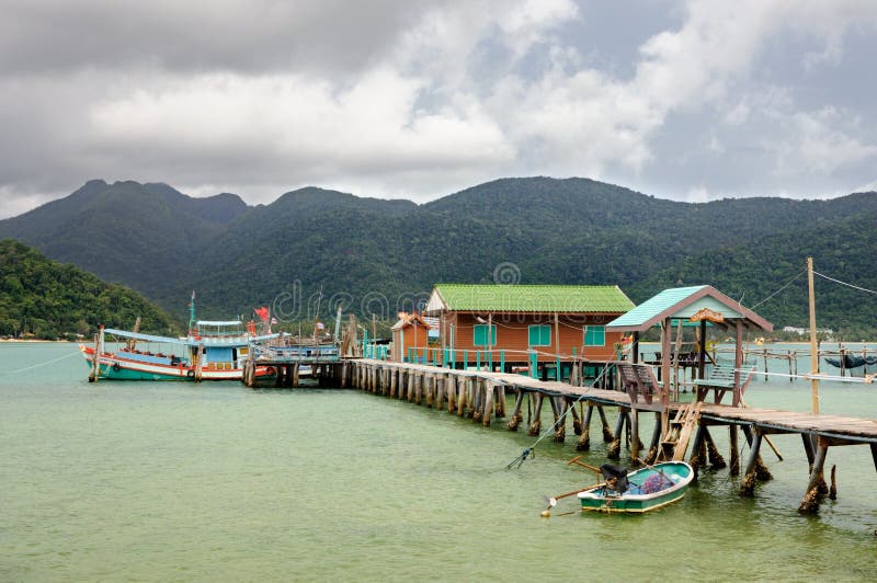 Paisaje tropical con el mar tropical de la turquesa, el barco de pesca, la casa en el agua, el embarcadero de madera y la isla de imagen de archivo libre de regalías Paisaje tropical con el mar tropical de la turquesa, el barco de pesca, la casa en el agua, el embarcadero de madera y la isla de imagen de archivo libre de regalías
