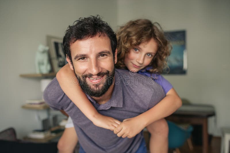 Paizinho de sorriso que dá a seu filho um reboque em casa fotografia de stock Paizinho de sorriso que dá a seu filho um reboque em casa fotografia de stock