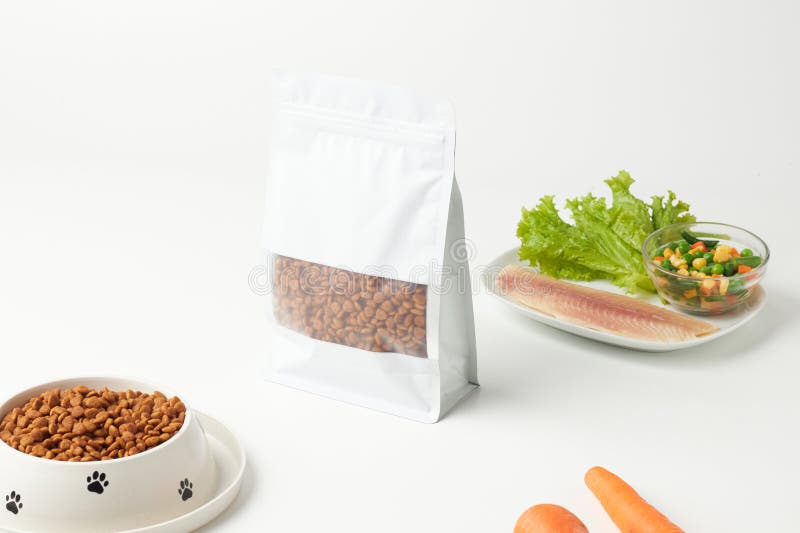 Paket med torrfoder för sällskapsdjur bredvid färska grönsaker och kött på en ren yta arkivbilder