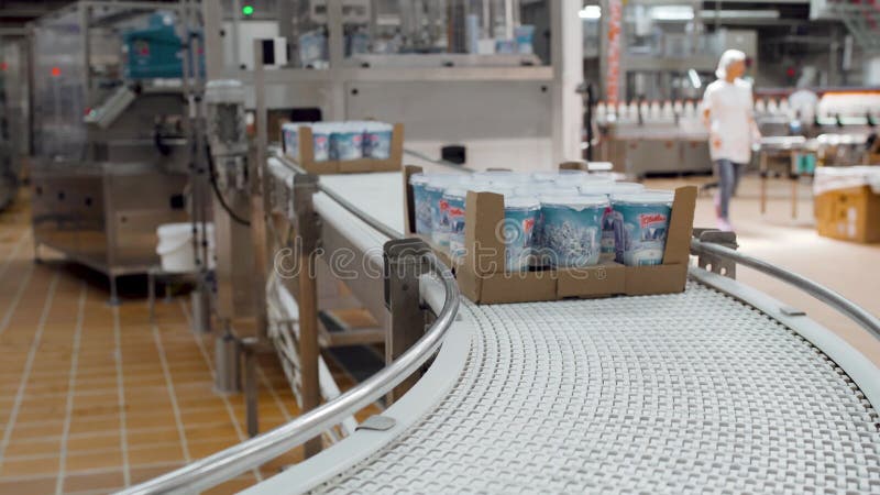 Pakete von Milcherzeugnissen gehen auf ein Förderband. Nahaufnahme von Plastikschalen mit Sahne.