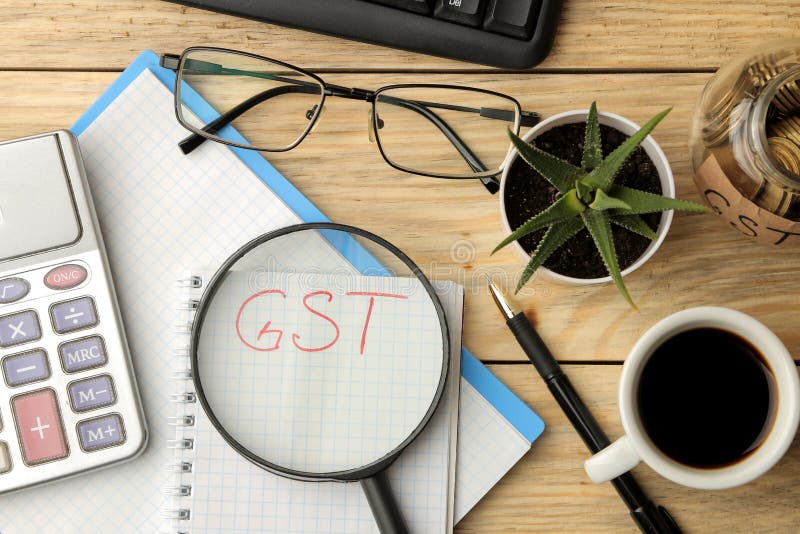 Palabra de GST en cuaderno debajo de la lupa y de la calculadora, pluma y café en fondo de madera marrón Visión desde arriba imagenes de archivo Palabra de GST en cuaderno debajo de la lupa y de la calculadora, pluma y café en fondo de madera marrón Visión desde arriba imagenes de archivo