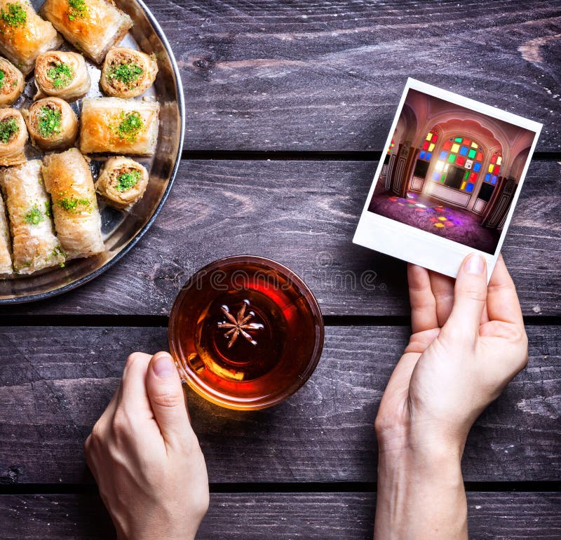 Hands with photo of Rajasthan palace and badyan tea near Turkish baklava on wooden background. Hands with photo of Rajasthan palace and badyan tea near Turkish baklava on wooden background