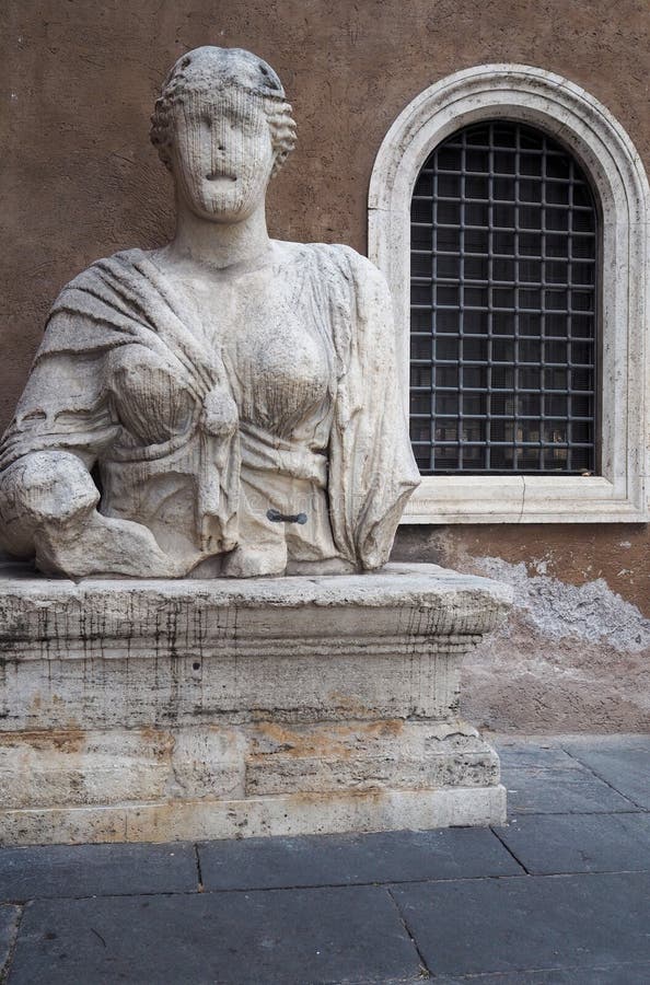 Madama Lucrezia sited on a plinth in the corner of a piazza between the Palazzo Venezia and the basilica of St. Mark in Rome, Italy. Madama Lucrezia is a colossal Roman bust, about 3 meters high.The statue is badly disfigured, and the original subject cannot be identified with certainty, but may represent the Egyptian goddess Isis. She is is one of the five `talking statues` of Rome and the only female sculpture. Madama Lucrezia sited on a plinth in the corner of a piazza between the Palazzo Venezia and the basilica of St. Mark in Rome, Italy. Madama Lucrezia is a colossal Roman bust, about 3 meters high.The statue is badly disfigured, and the original subject cannot be identified with certainty, but may represent the Egyptian goddess Isis. She is is one of the five `talking statues` of Rome and the only female sculpture.