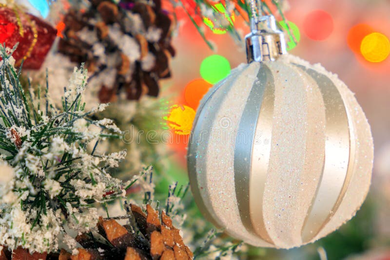 Palla brillante bianca che appende su un ramo innevato di un albero di Natale contro un contesto delle luci multicolori immagine stock Palla brillante bianca che appende su un ramo innevato di un albero di Natale contro un contesto delle luci multicolori immagine stock