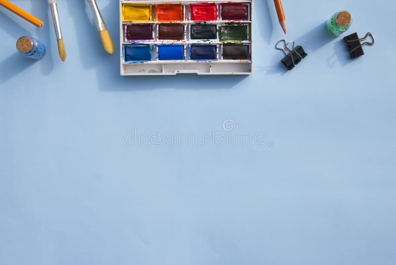 Pallette of watercolor paints and paintbrushes for painting. Blue background. Copy space.