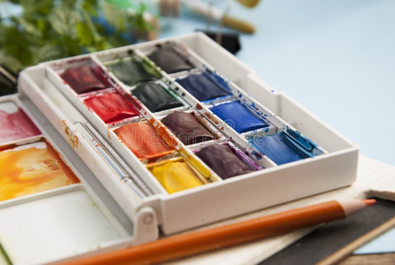 Pallette of watercolor paints and paintbrushes for painting. Blue background. Selective focus.