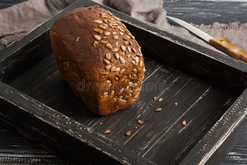 Pan de Rye con las semillas de girasol en una bandeja negra de madera, servilleta, cuchillo fotos de archivo Pan de Rye con las semillas de girasol en una bandeja negra de madera, servilleta, cuchillo fotos de archivo