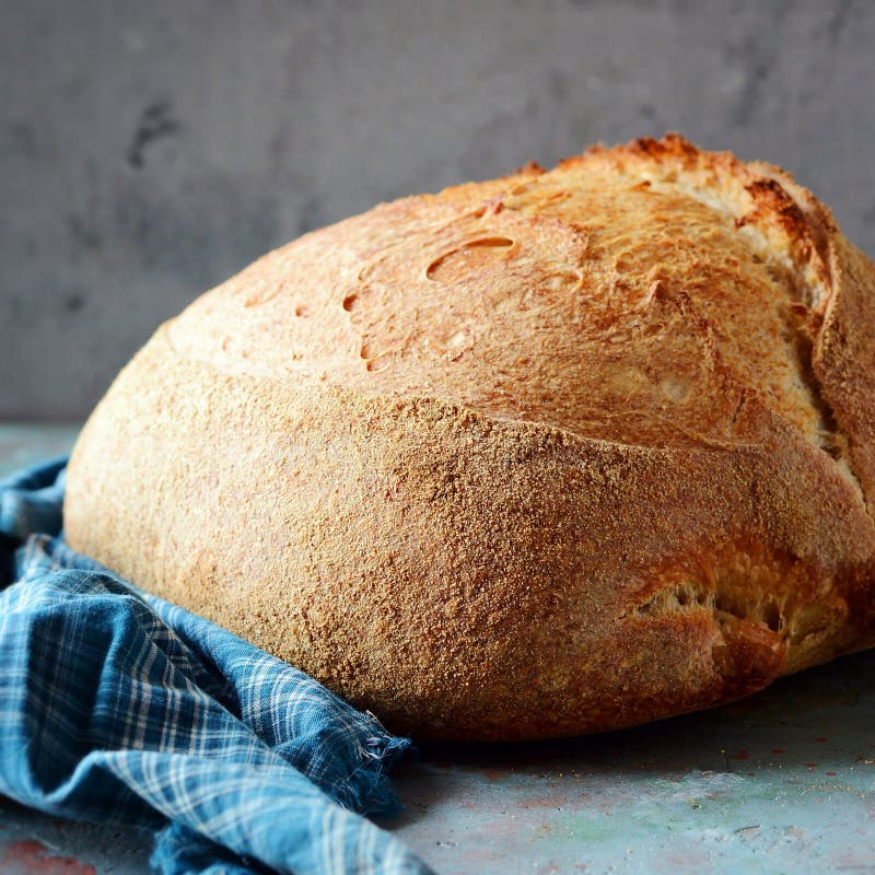 Pan recientemente cocido hecho en casa del país hecho de trigo y de harina entera del grano en un fondo gris-azul imagen de archivo libre de regalías Pan recientemente cocido hecho en casa del país hecho de trigo y de harina entera del grano en un fondo gris-azul imagen de archivo libre de regalías