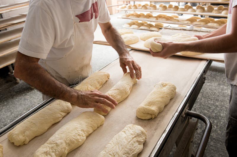 Panaderos que ponen el pan a una banda para el horno fotografía de archivo Panaderos que ponen el pan a una banda para el horno fotografía de archivo
