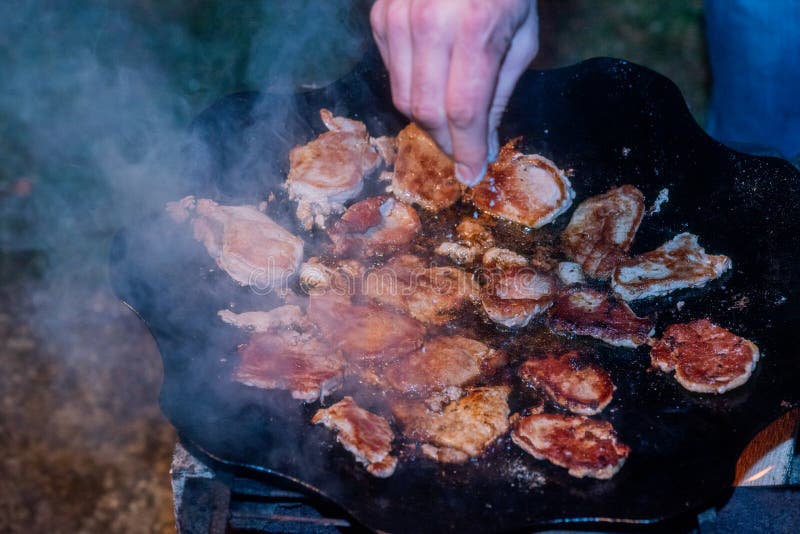 Pancetta tagliata fresca cotta su un fuoco da campeggio. la carne è fritta in una pentola sopra il fuoco