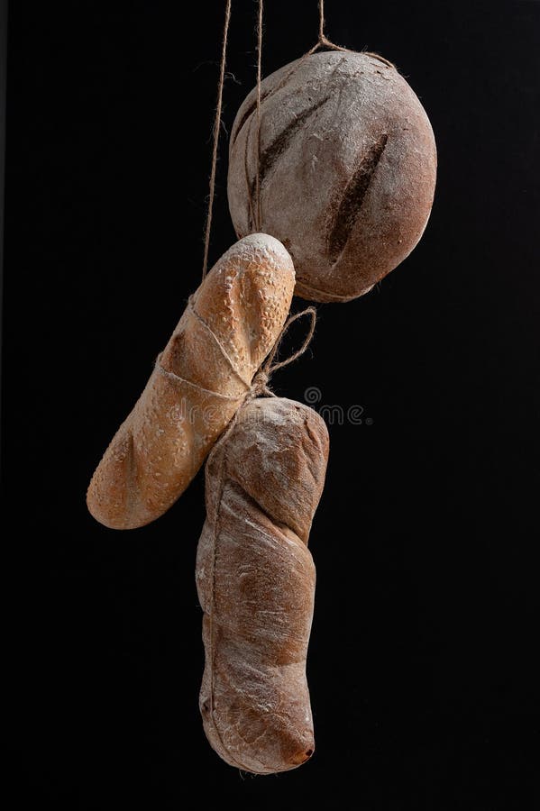 Pane fresco di varie forme appeso alle corde su fondo nero immagini stock